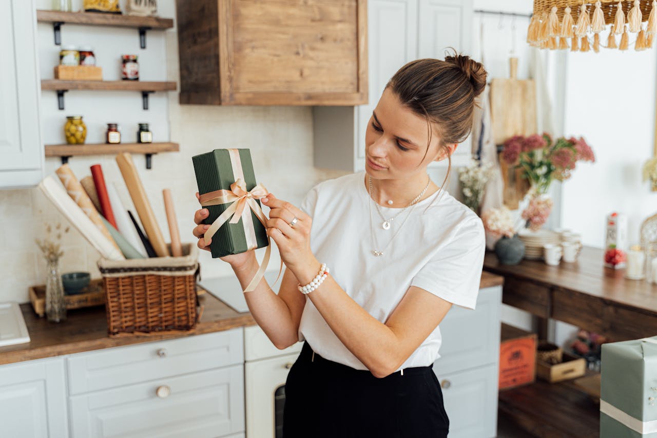 A woman wrapping a gift box with ribbon in a cozy kitchen, capturing a warm and creative atmosphere.